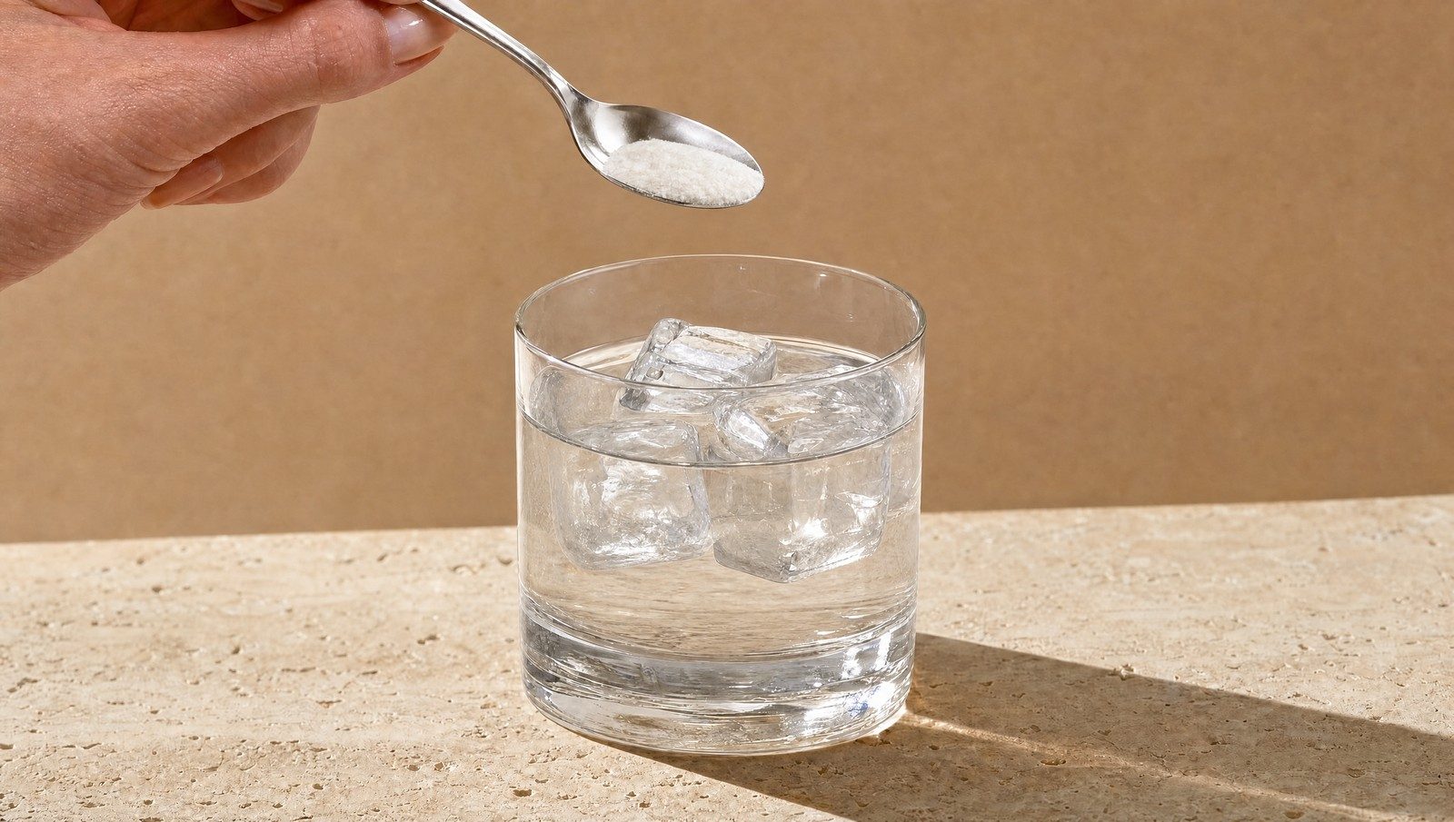 Ein Teelöffel gibt ein weißes Pulver in ein Glas Wasser mit Eiswürfeln