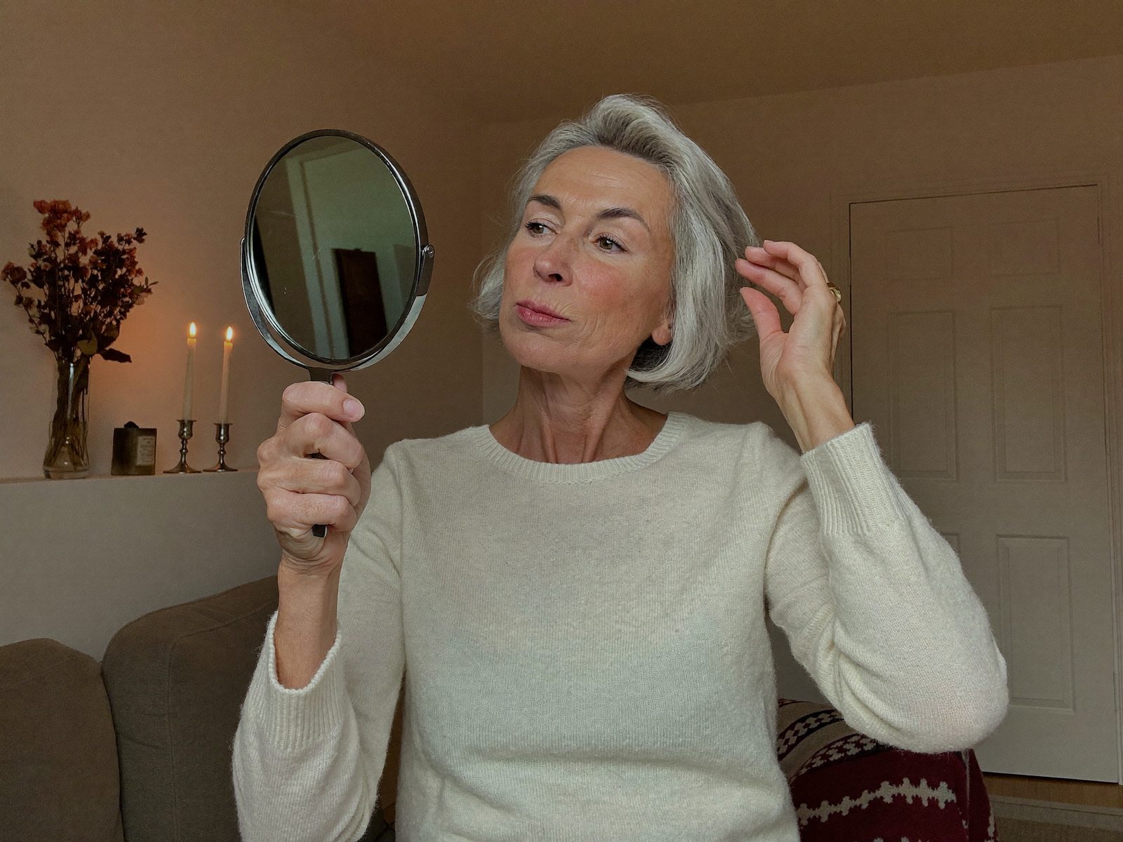 Femme qui regarde sa peau et ses cheveux dans un miroir à main, d'un œil critique